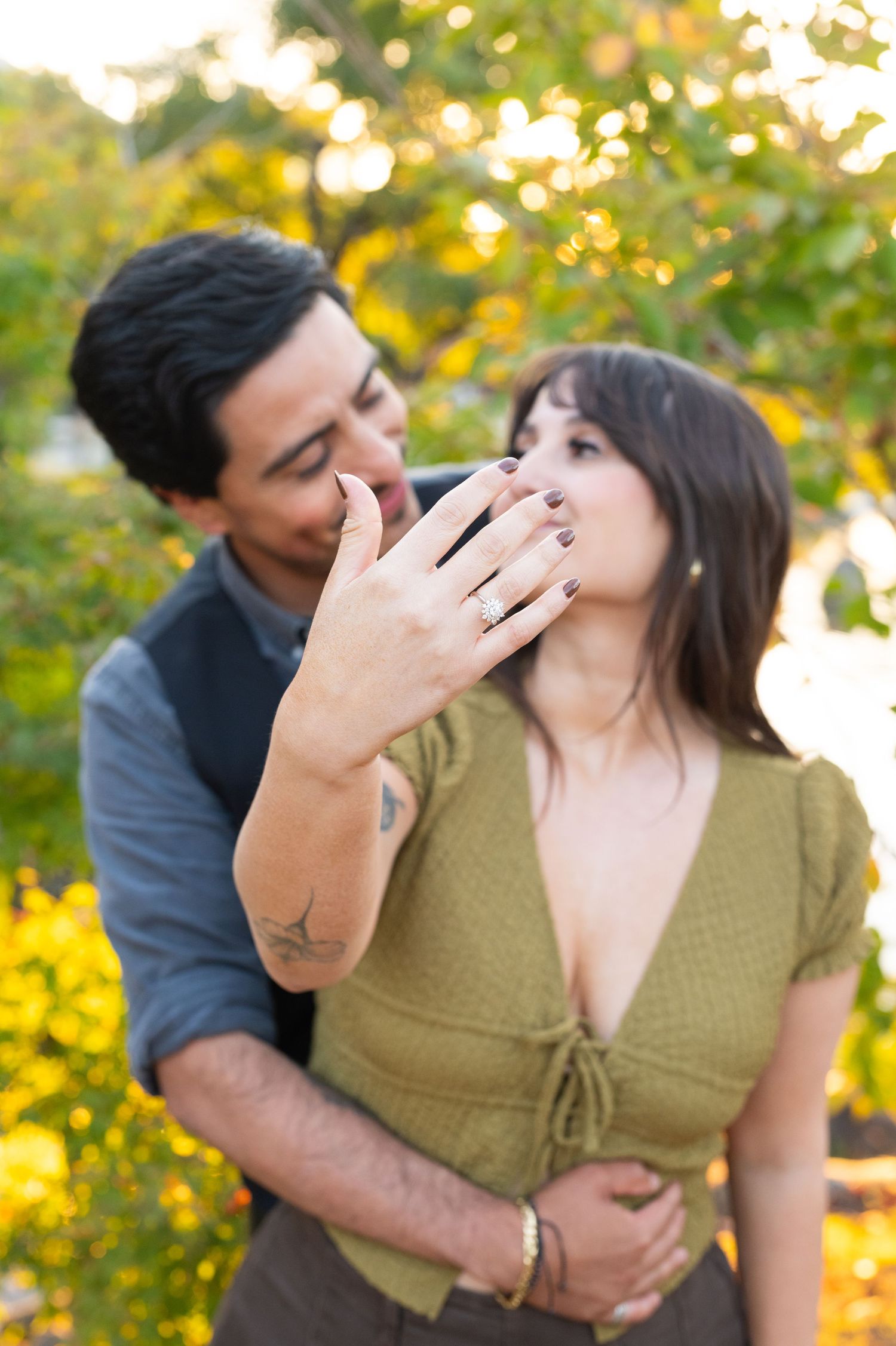 Newly engaged couple showing off diamond engagement ring with golden bokeh background in a garden.