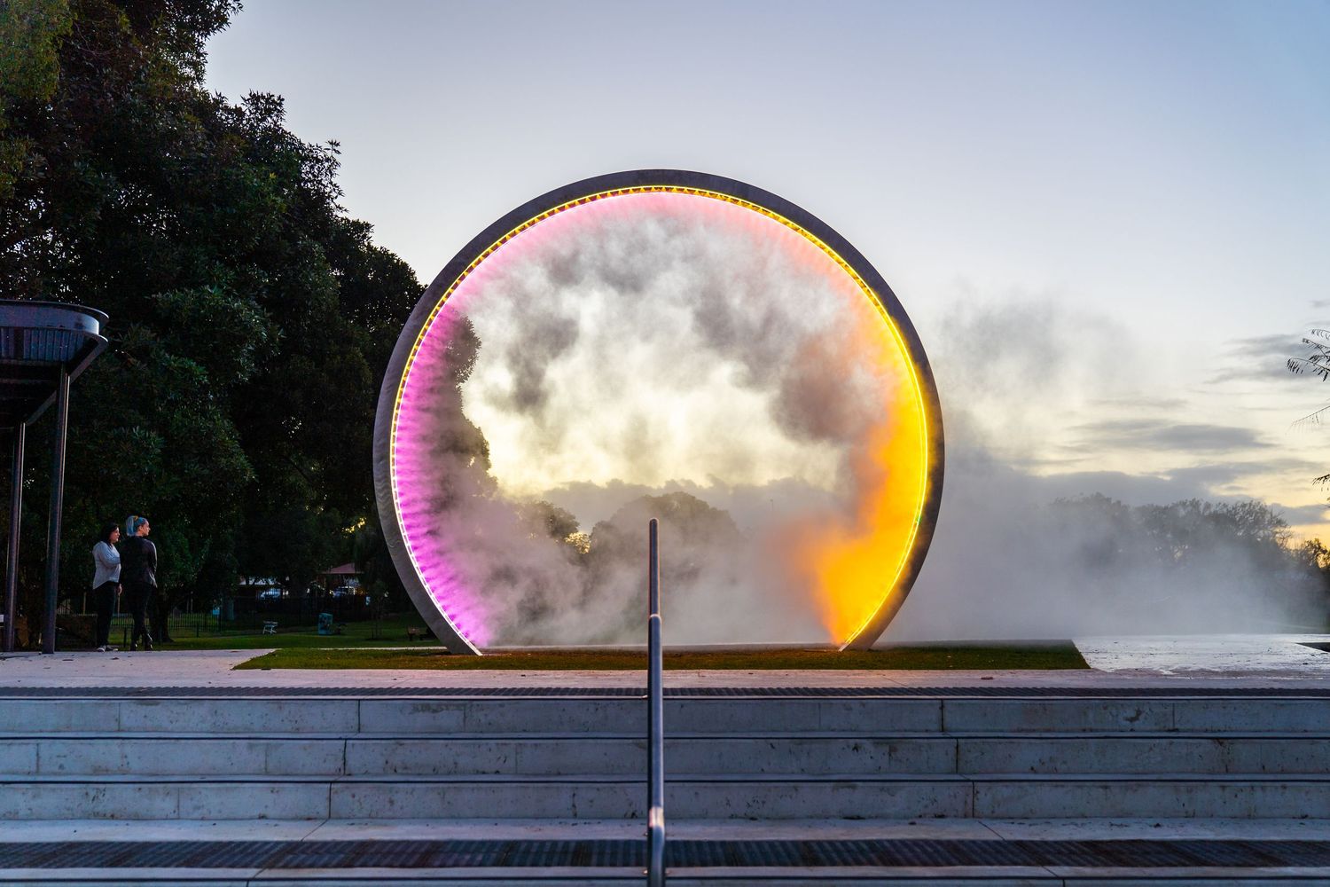 Modern architectural structure with pink illuminated arch at dusk.