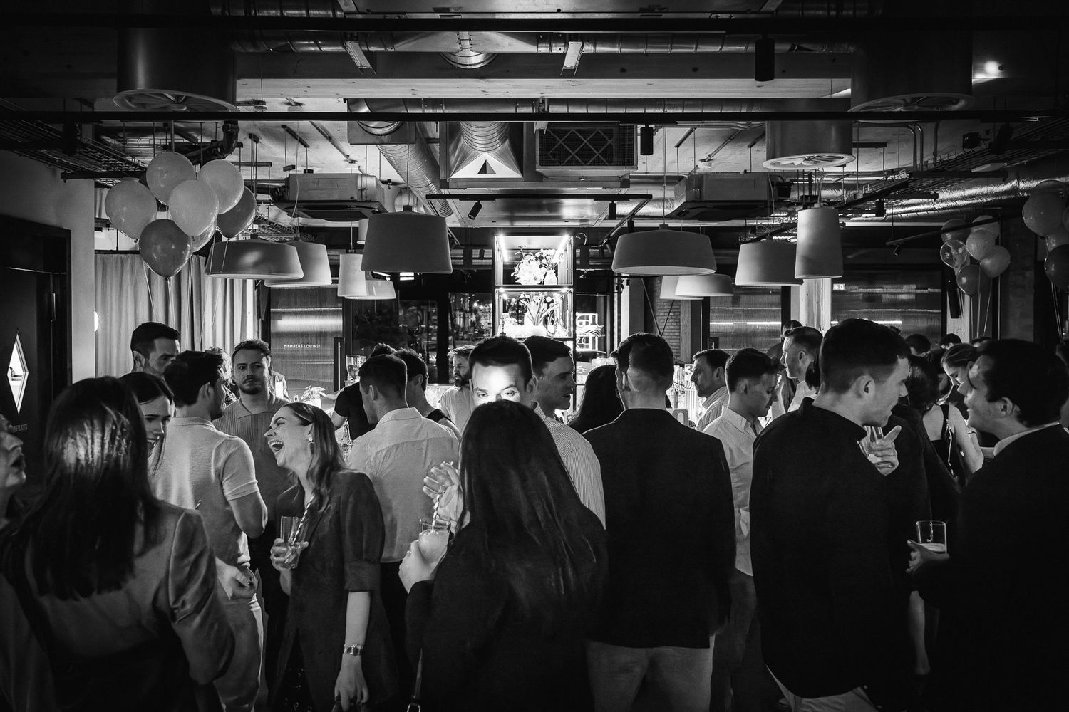 Black and white photo of crowded networking event in modern industrial space.
