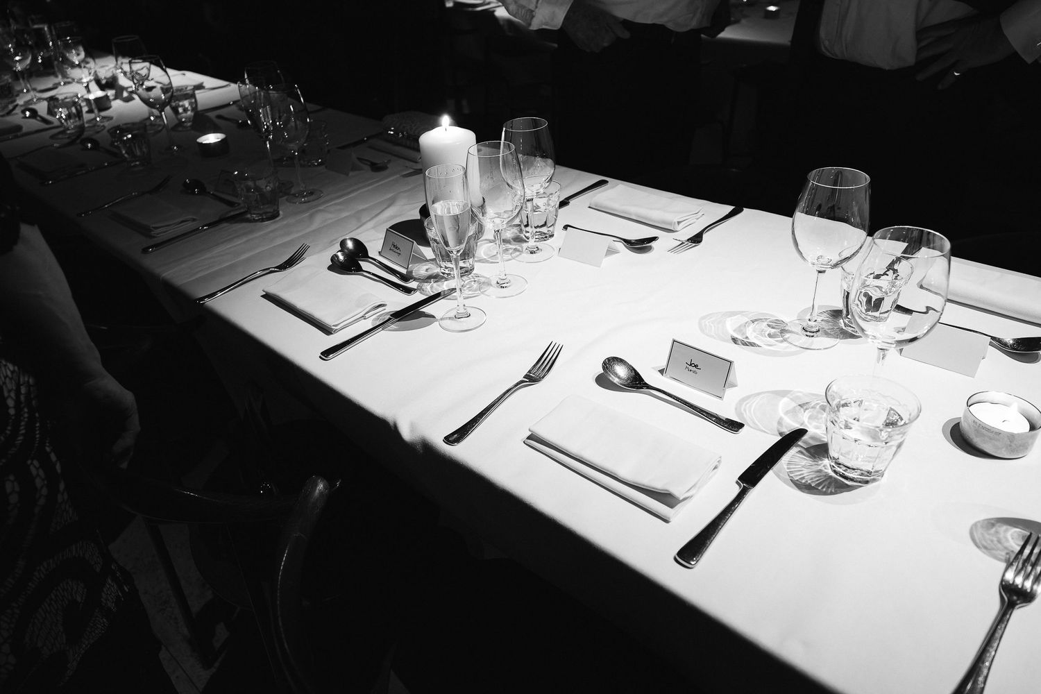 Black and white image of formal table setting with glasses and cutlery.