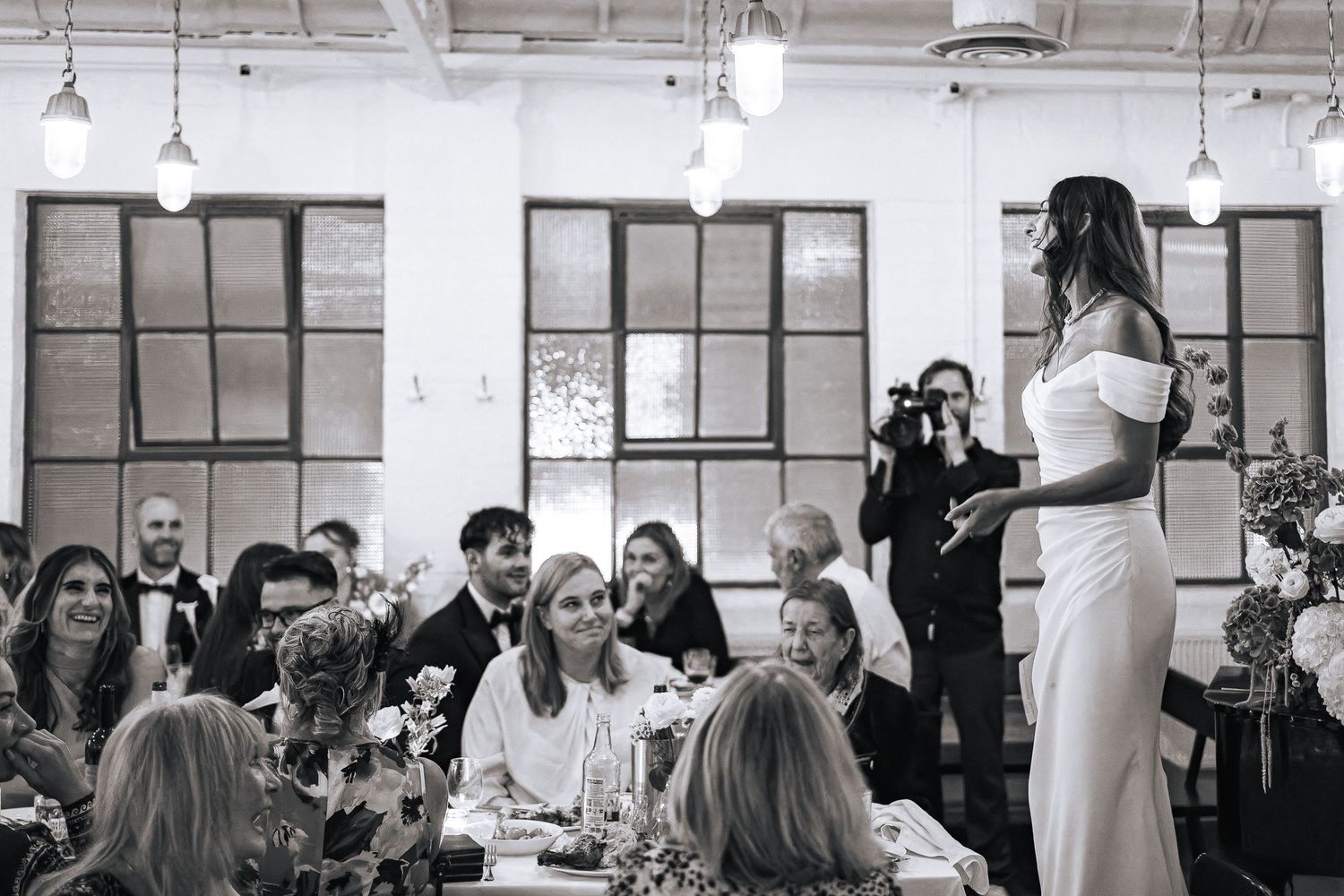 Modern white event space filled with guests seated at long tables for a celebration.