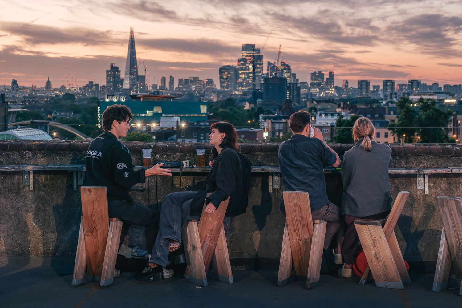 Wooden chairs overlooking a city skyline at sunset with skyscrapers in the background.