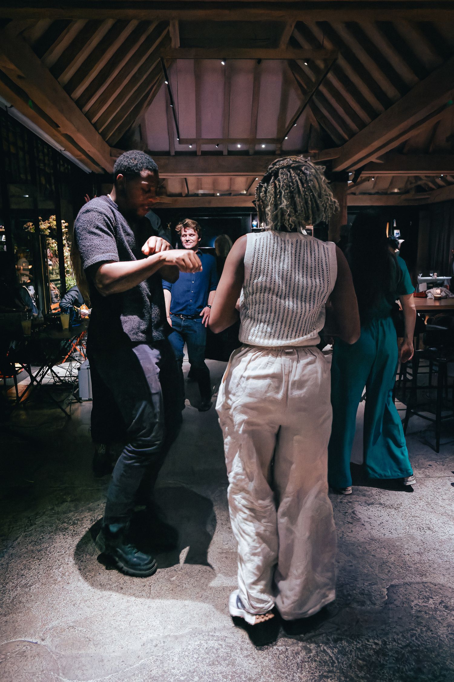 Guests dancing and mingling at an indoor reception venue with rustic wooden beams.