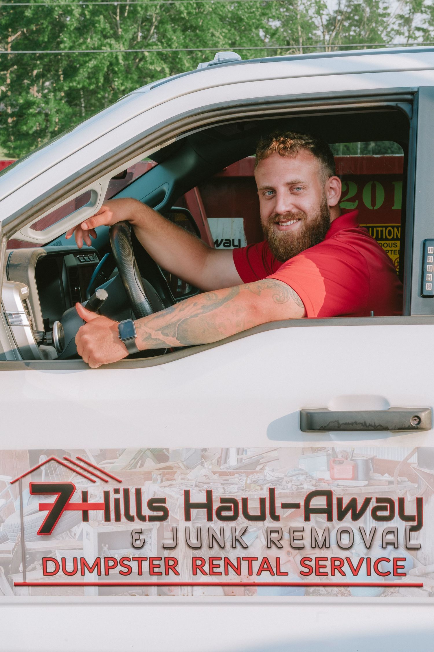 Junk removal service workers smile from company vehicles displaying 7 Hills Haul-Away branding.