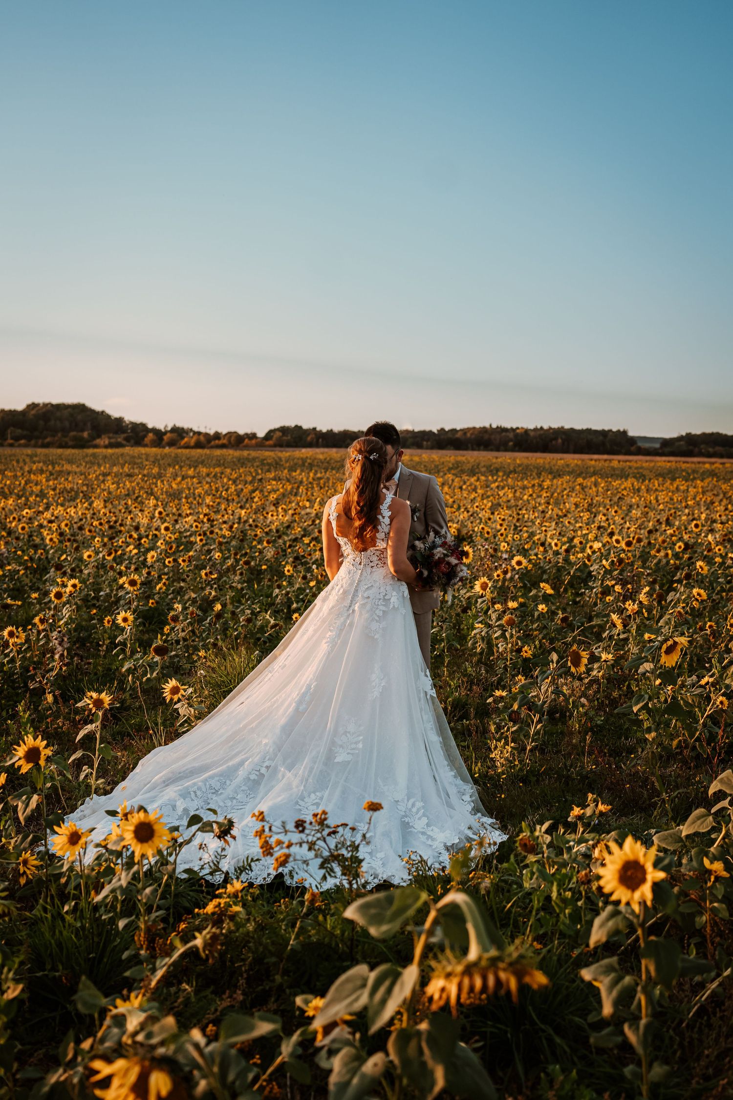 Couple embracing on a hilltop at sunset with tall pine trees framing the romantic mountain landscape.