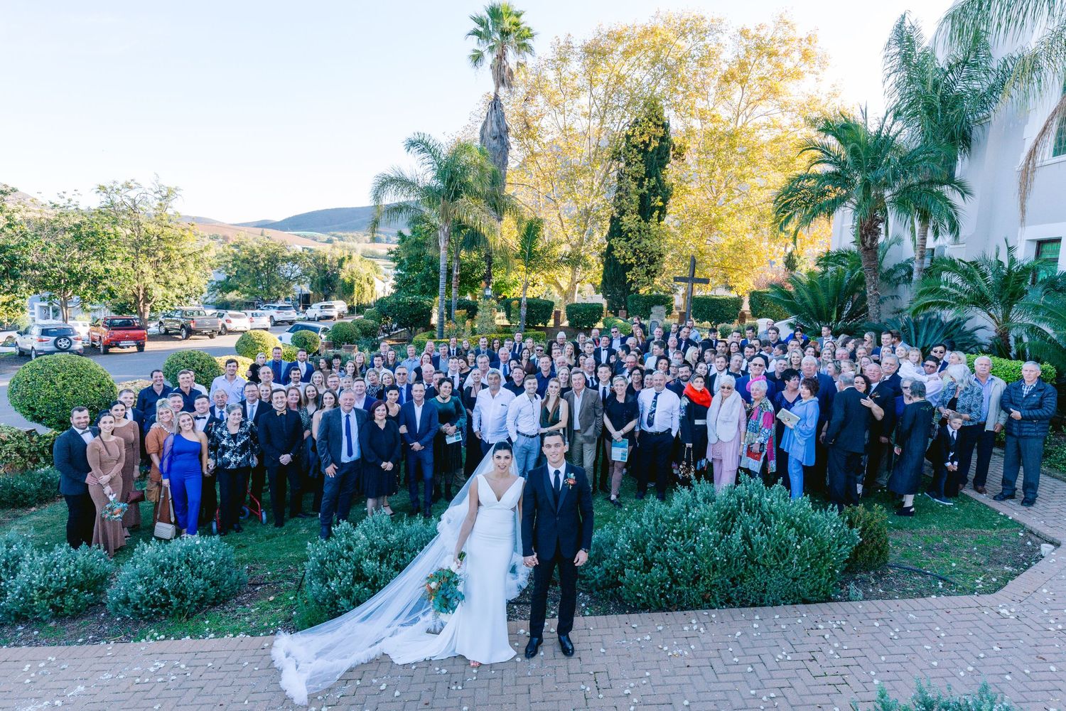 Wedding guests gather on a lush garden patio during an outdoor ceremony at sunset.