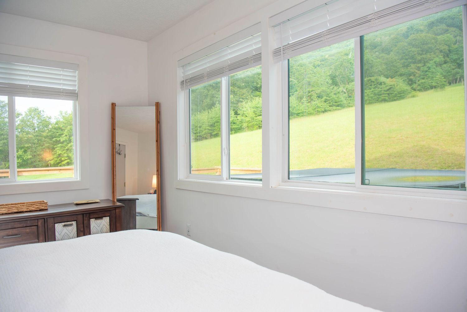 Modern bedroom with large windows overlooking green hills and natural scenery.
