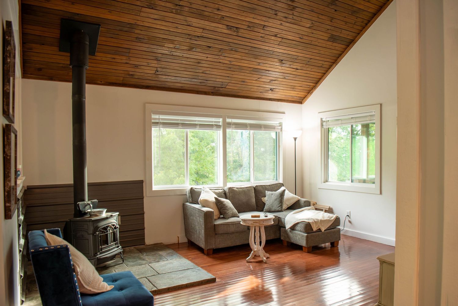 Modern living room interior with wood plank ceiling, large windows, and grey furniture in an open concept space.