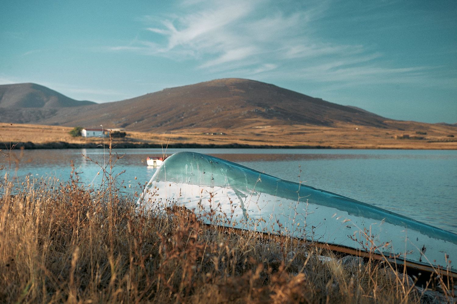 Panoramic view of a serene turquoise lake surrounded by brown mountains under a bright blue sky with wispy clouds.