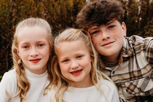 A group poses together outdoors in coordinated neutral tones and plaid for a casual autumn family portrait.