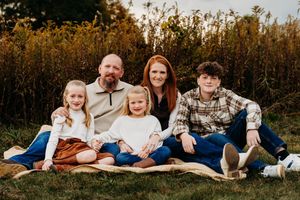A family group relaxes together outdoors wearing coordinated white and denim outfits during a golden hour photo session.