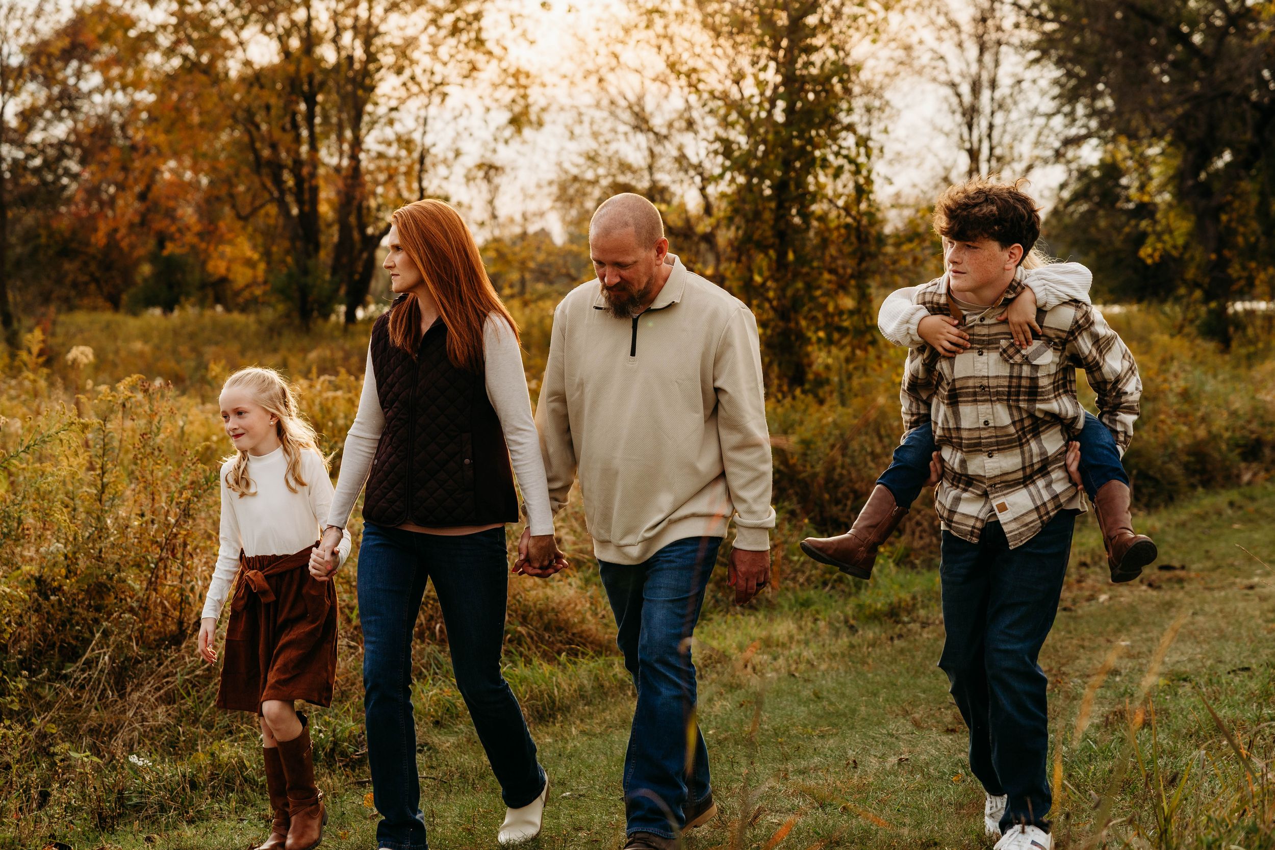 Family walking together through a golden autumn field at sunset during a lifestyle photo session.