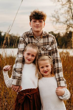 Children wearing plaid and white outfits pose together in a golden autumn field at sunset.