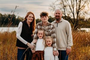 Family walking through golden autumn field at sunset during outdoor photo session.