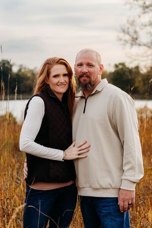 A couple embraces lovingly in a golden field during sunset, wearing contrasting black and white outfits.