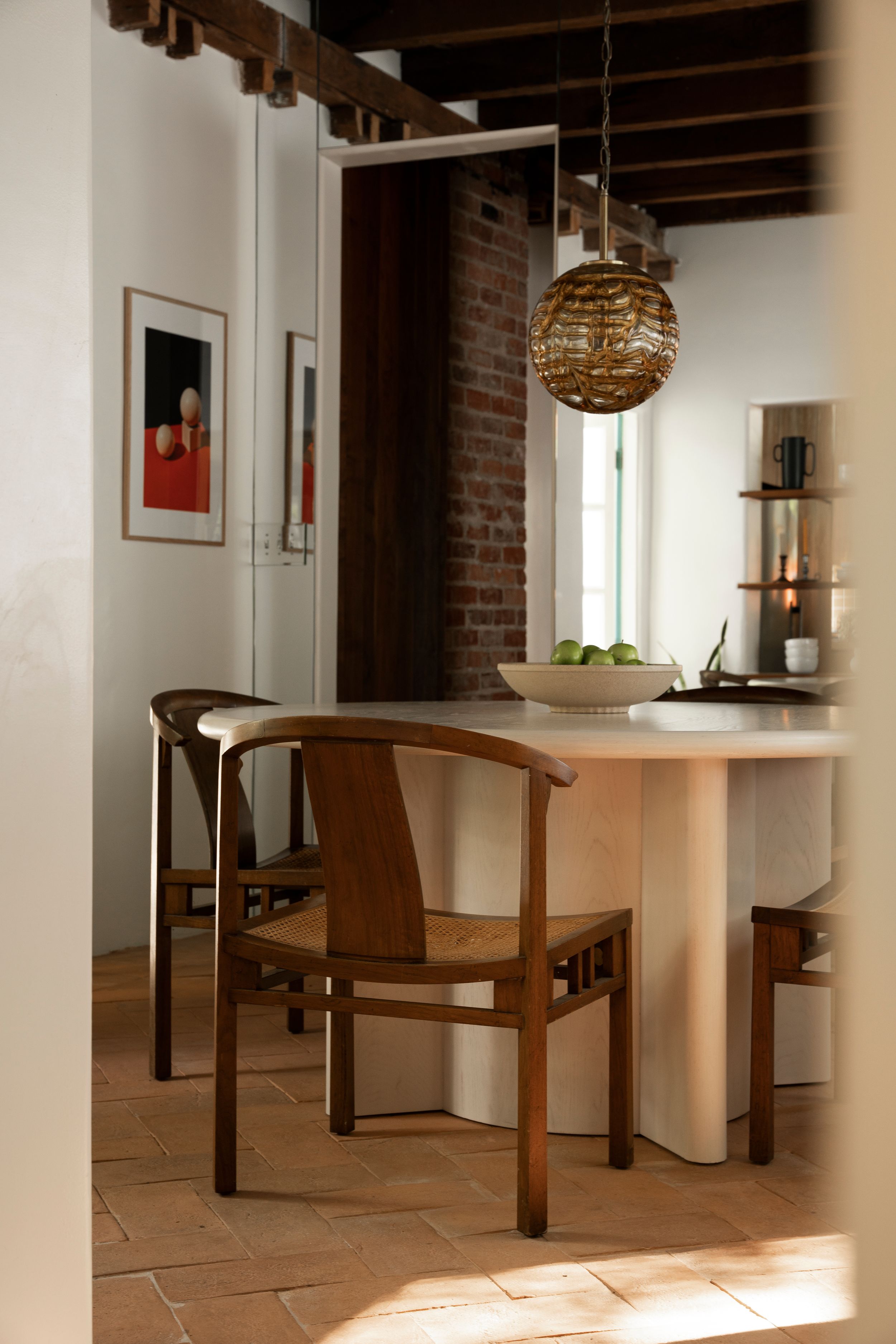 Modern dining area with white round table, wooden chairs, exposed brick wall and decorative sphere pendant light.