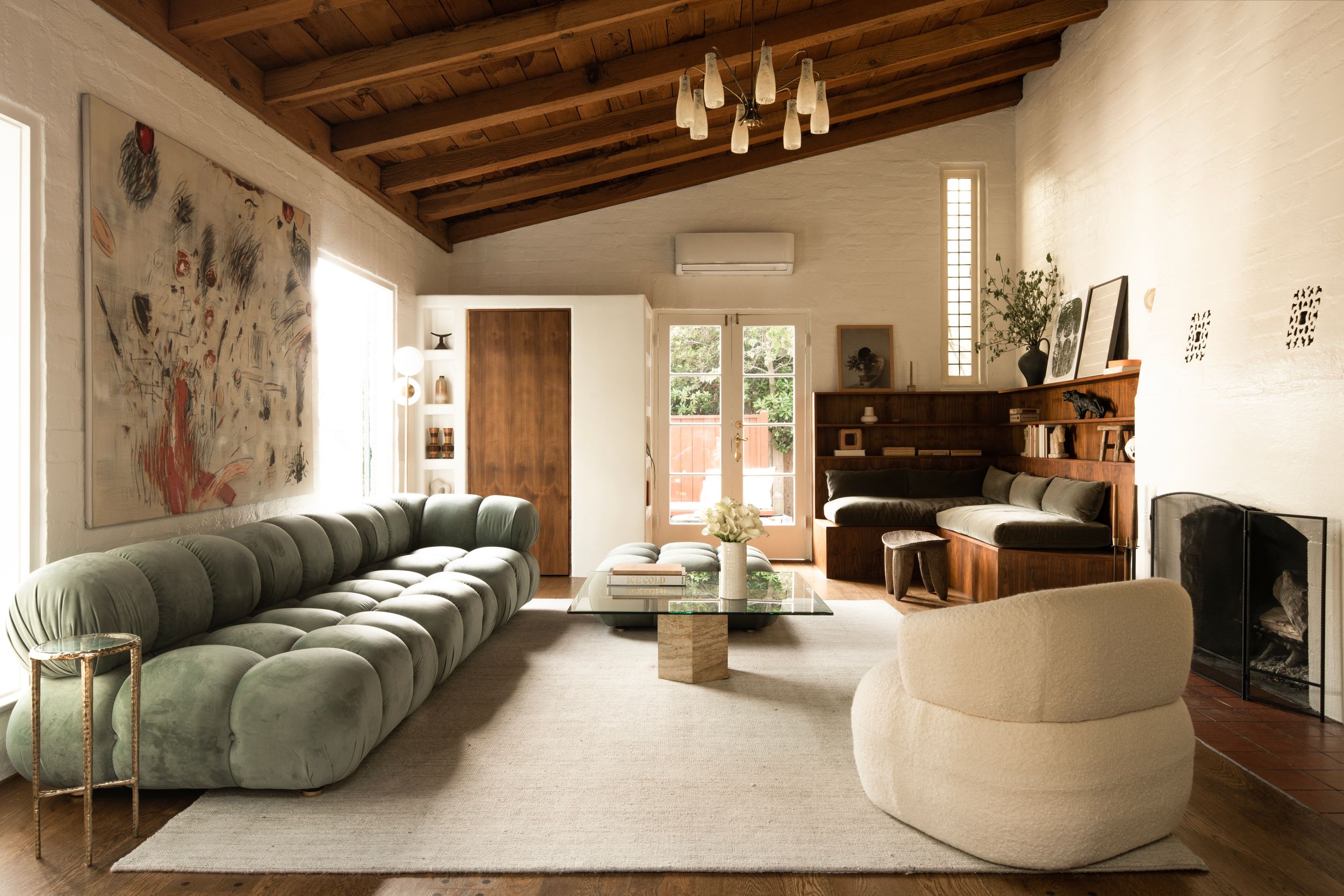 Modern living room features exposed wooden beams, white walls, and contemporary furniture in muted green and cream tones.