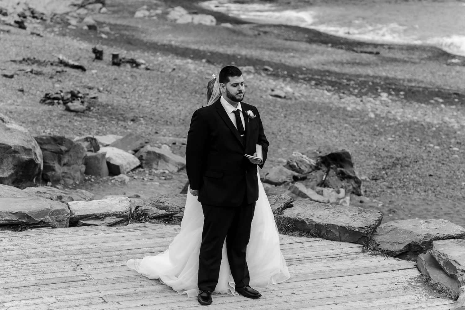 Wedding couple strolling on rugged beach shoreline in dramatic monochrome.