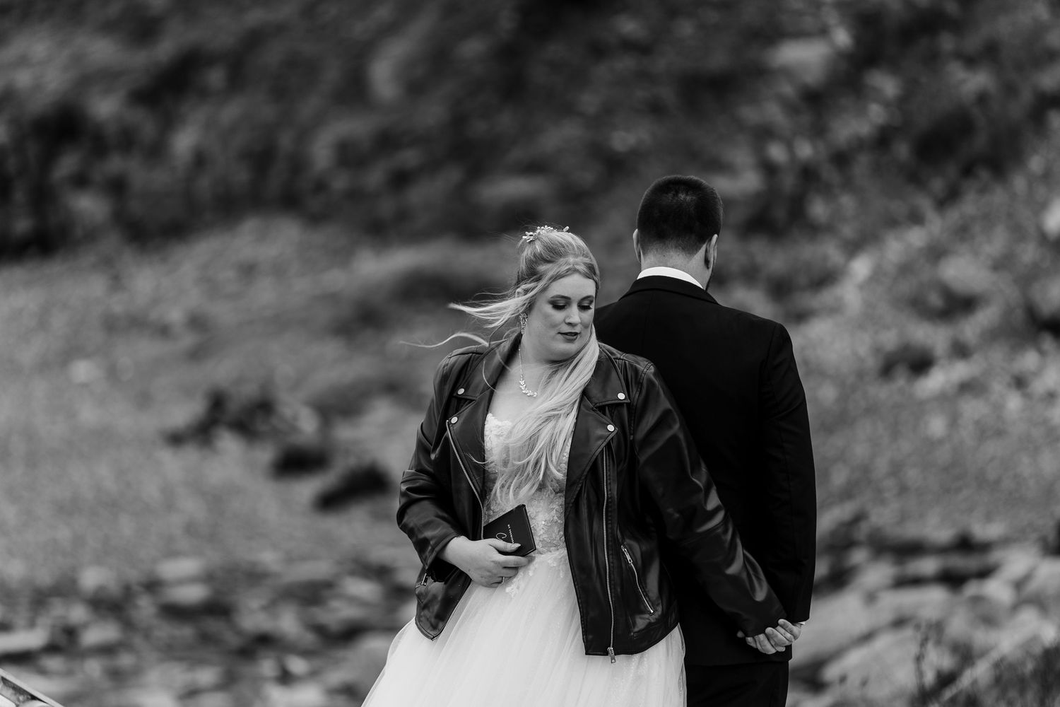 Romantic wedding portrait of couple walking together on dramatic seaside cliffs in black and white.