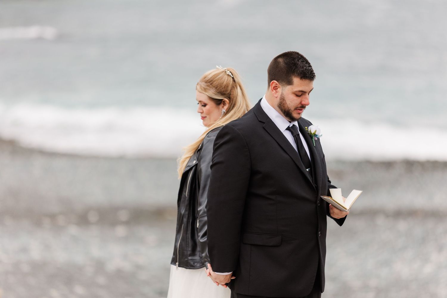A romantic moment between newlyweds on a beach boardwalk with rugged cliffs in the background.