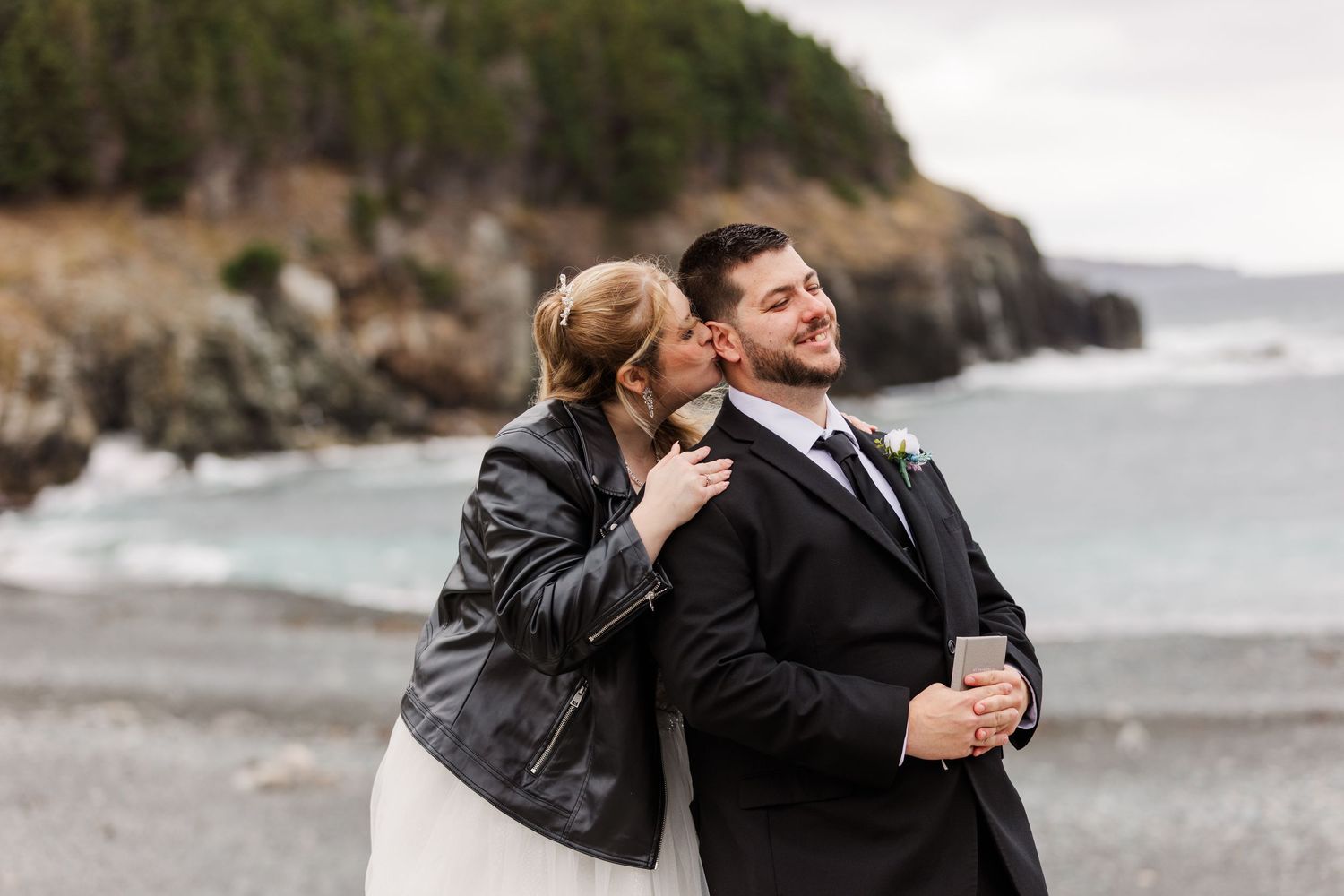 A couple shares intimate moments together while exploring a rocky beach coastline on an overcast day.