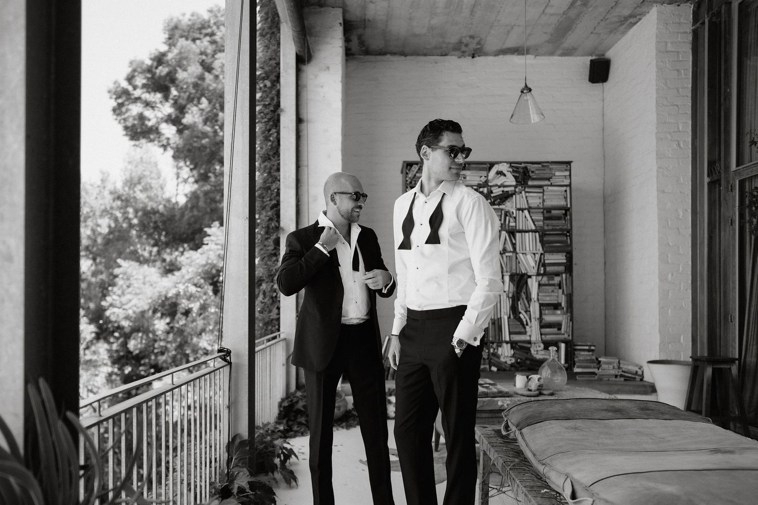 Two people in formal attire stand on a covered porch with railings in black and white photography.