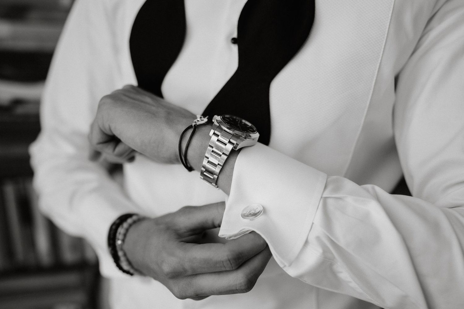 Black and white photo of hands adjusting a silver watch while wearing a white dress shirt and black vest.