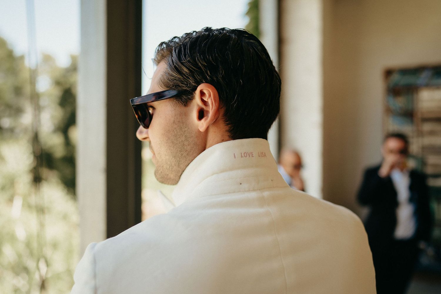 A person in a white shirt and sunglasses stands in a covered outdoor walkway with natural lighting.