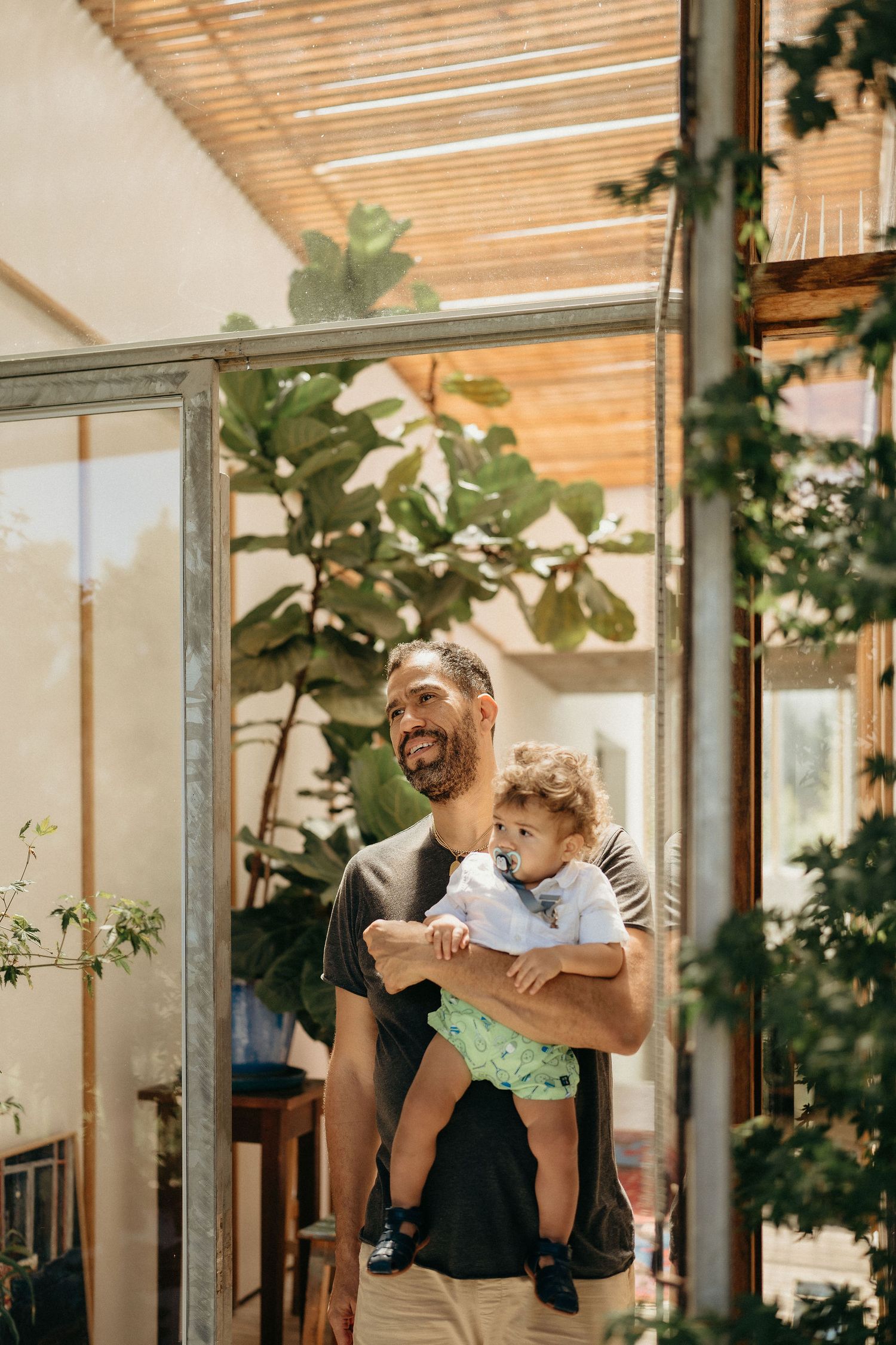 A joyful moment captured in a sunlit room with plants and wooden beams overhead.