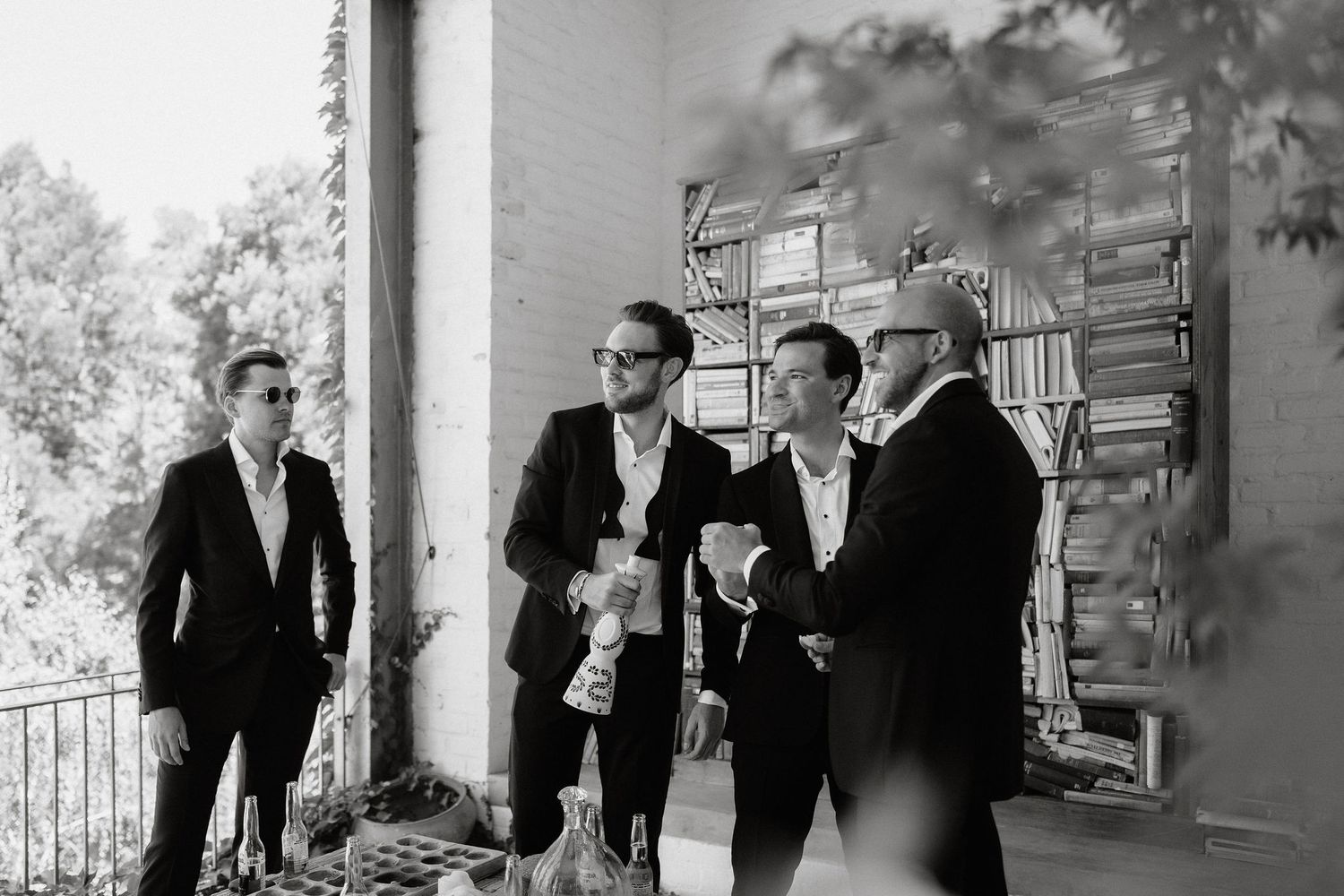 Wedding party members in formal attire gather for a casual moment on a porch.