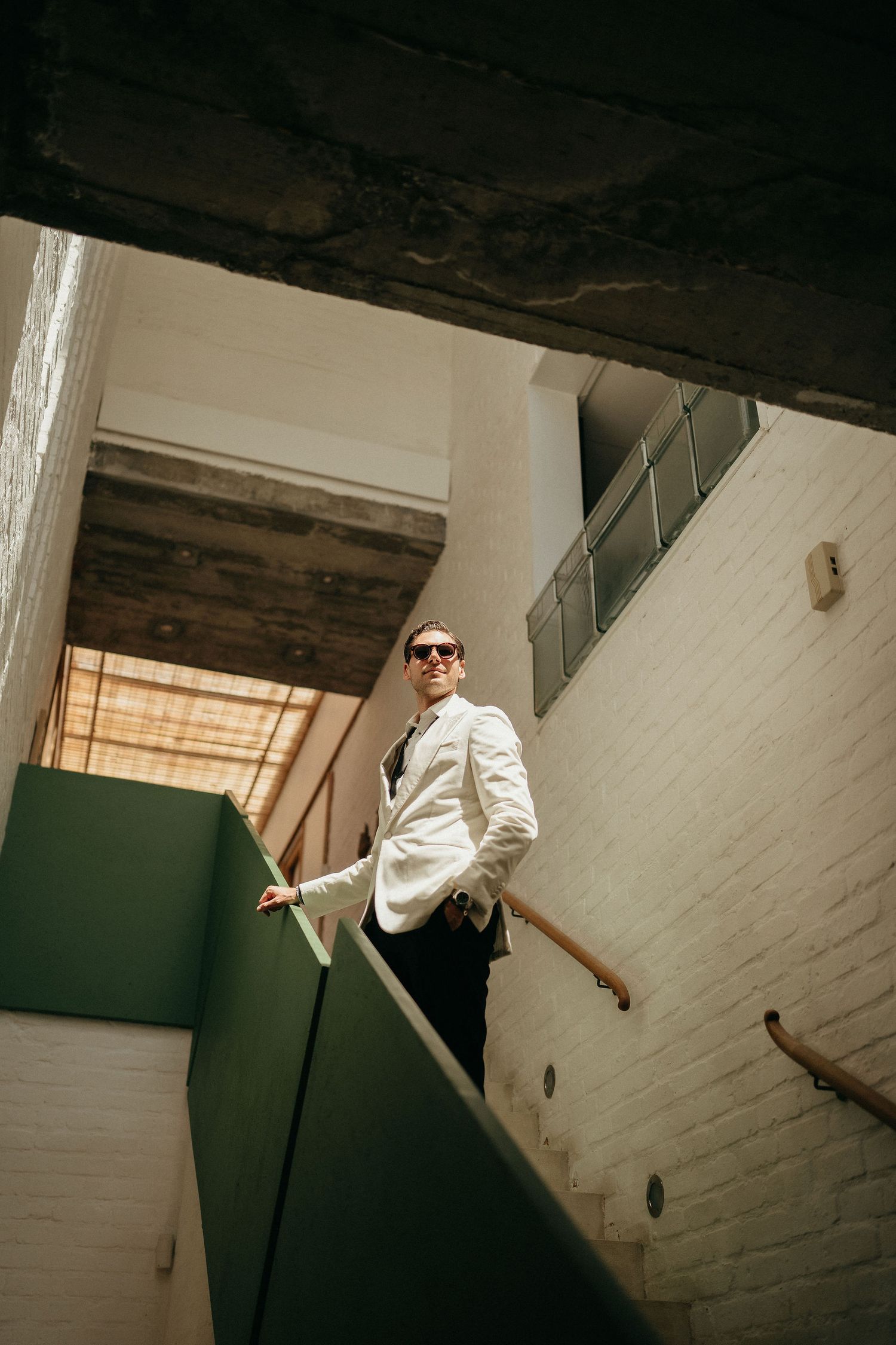 A person in sunglasses and white clothing performs a dynamic dance move against a white and green wall.
