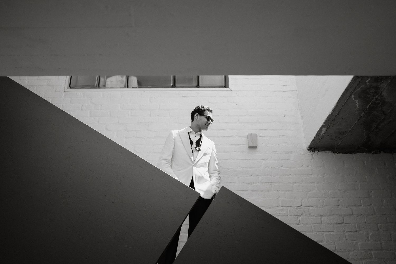 Black and white photograph of a person in a suit standing against a white brick wall.