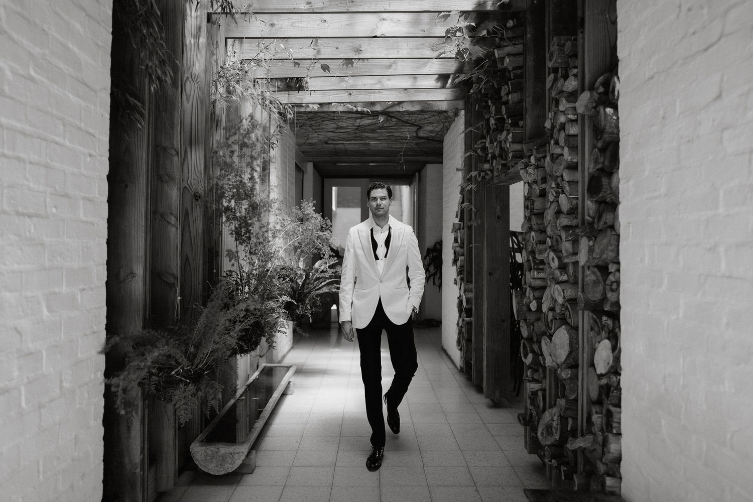A dramatic black and white photo shows a person walking down a long narrow corridor with light at the end.