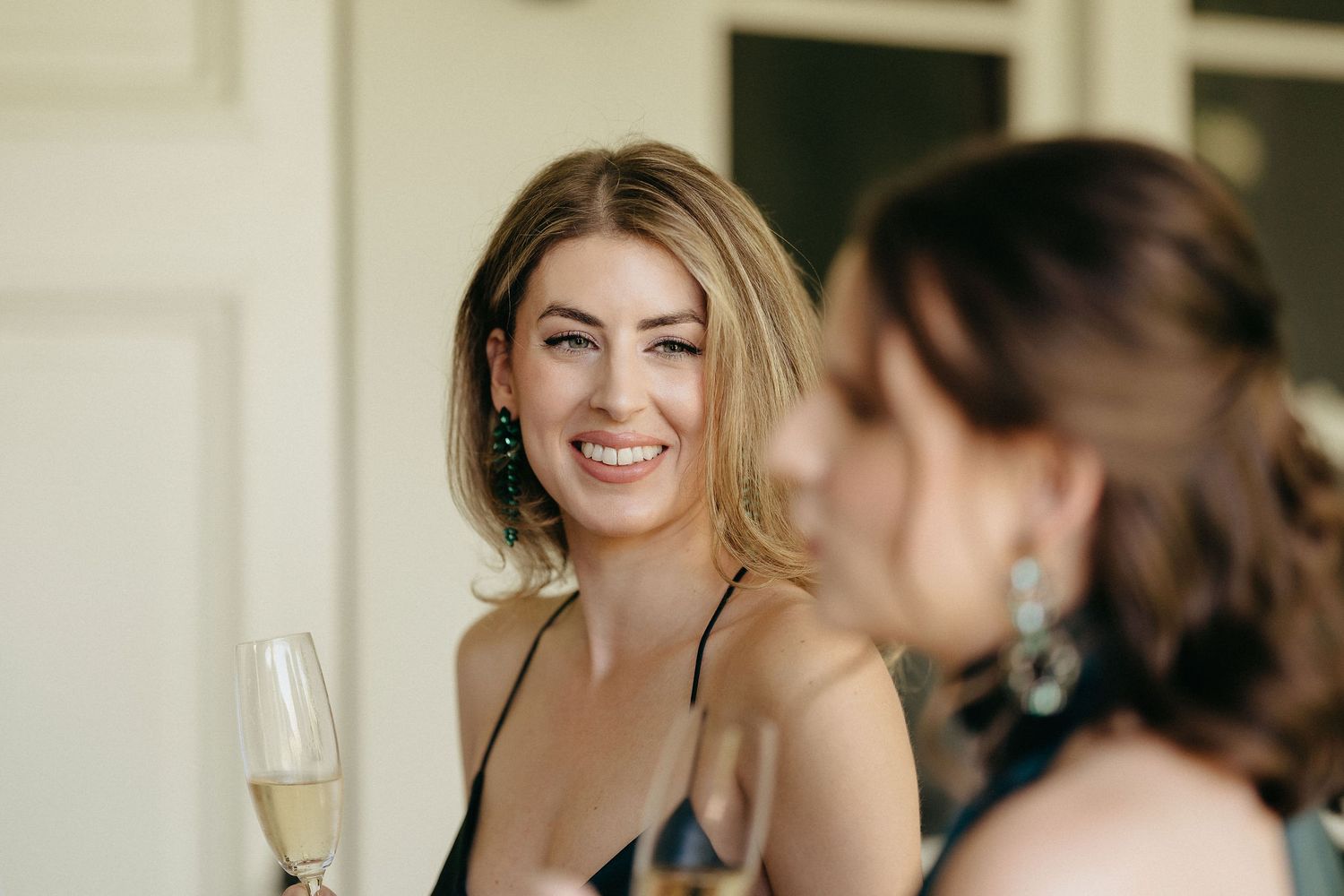 A group of people dressed in formal attire smile and laugh while holding champagne glasses at an elegant event.
