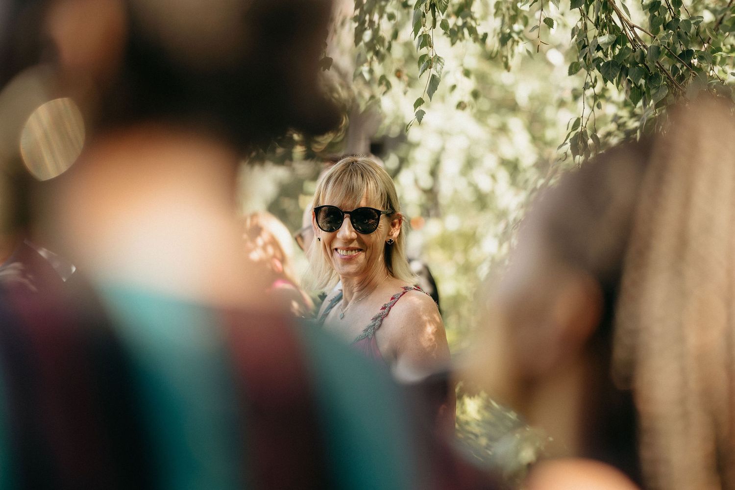 A group of people gather outdoors at a sunny event with natural bokeh lighting effects in the background.