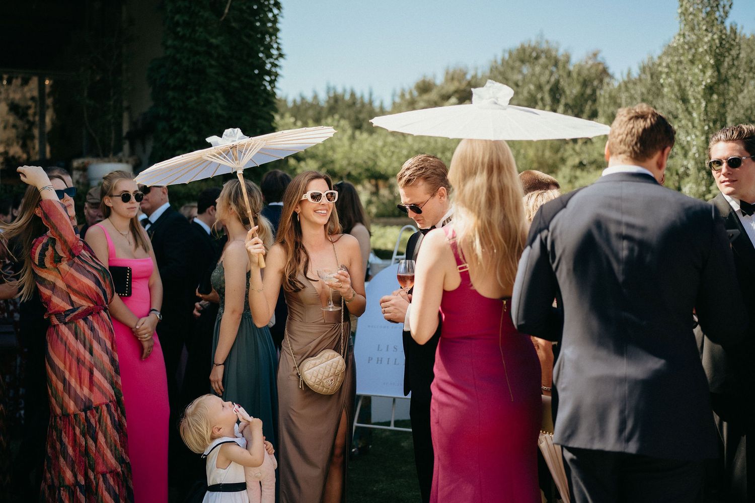 Guests mingle and socialize at an outdoor wedding reception on a sunny day.