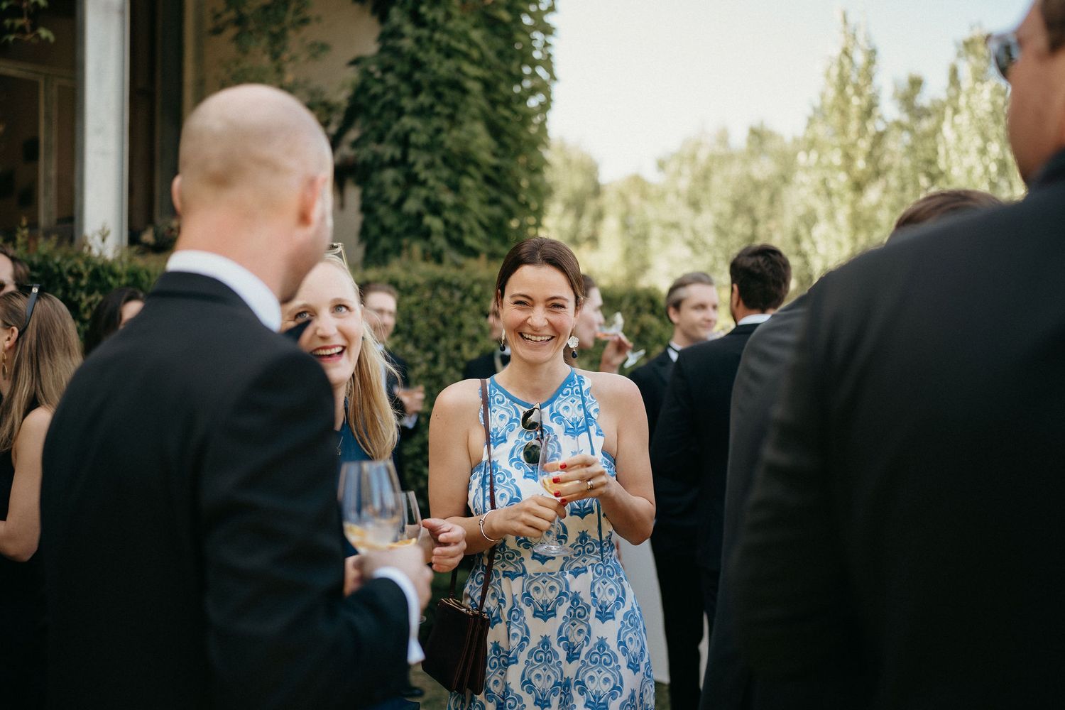 People celebrating and socializing at an outdoor wedding reception with drinks and laughter.