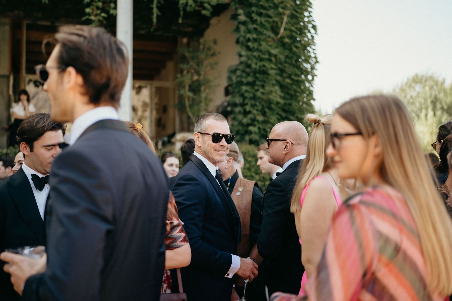 Wedding guests gathered in a garden setting with ivy-covered walls in the background.