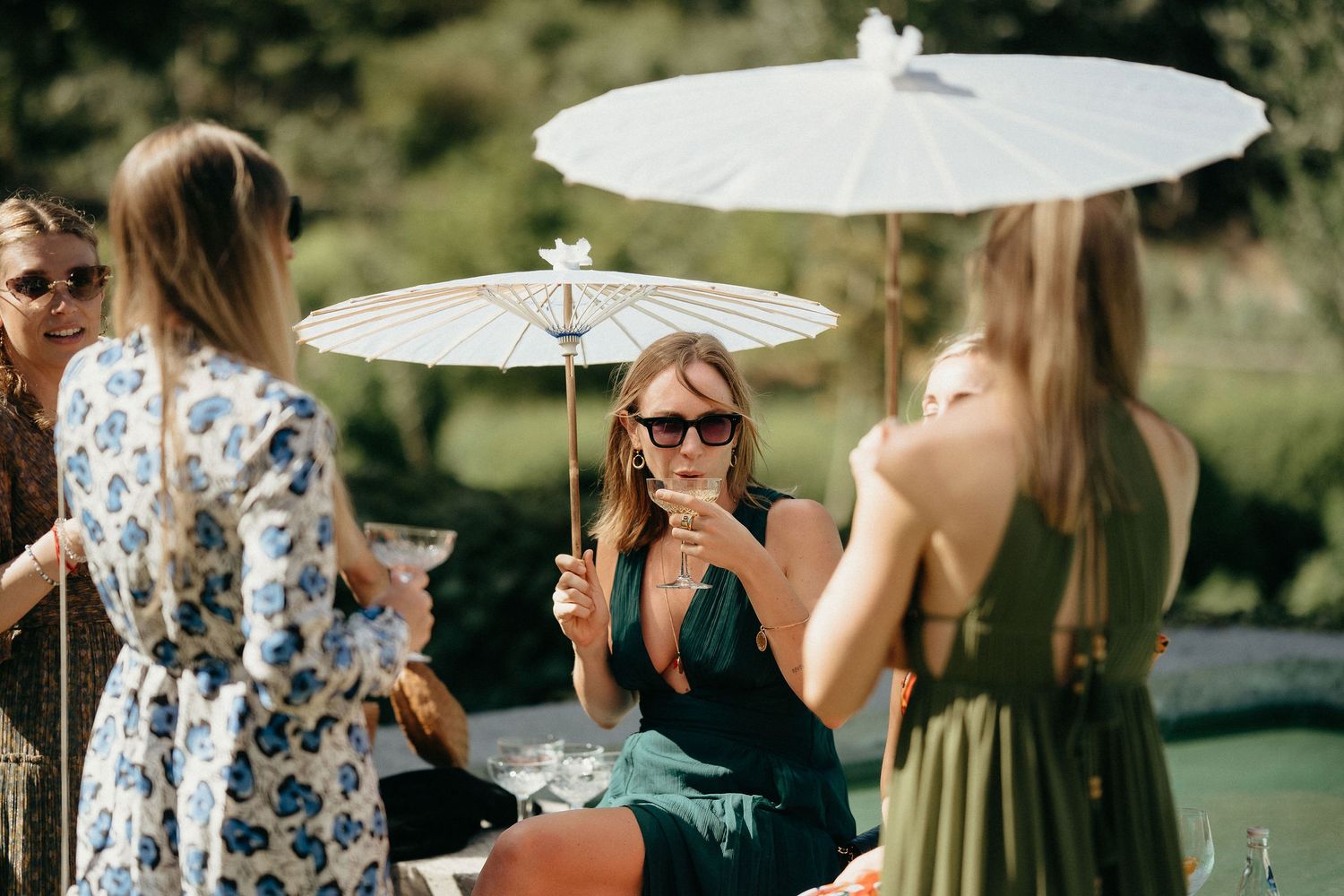 A group holding white parasols gathers outdoors at a sunny garden party event.