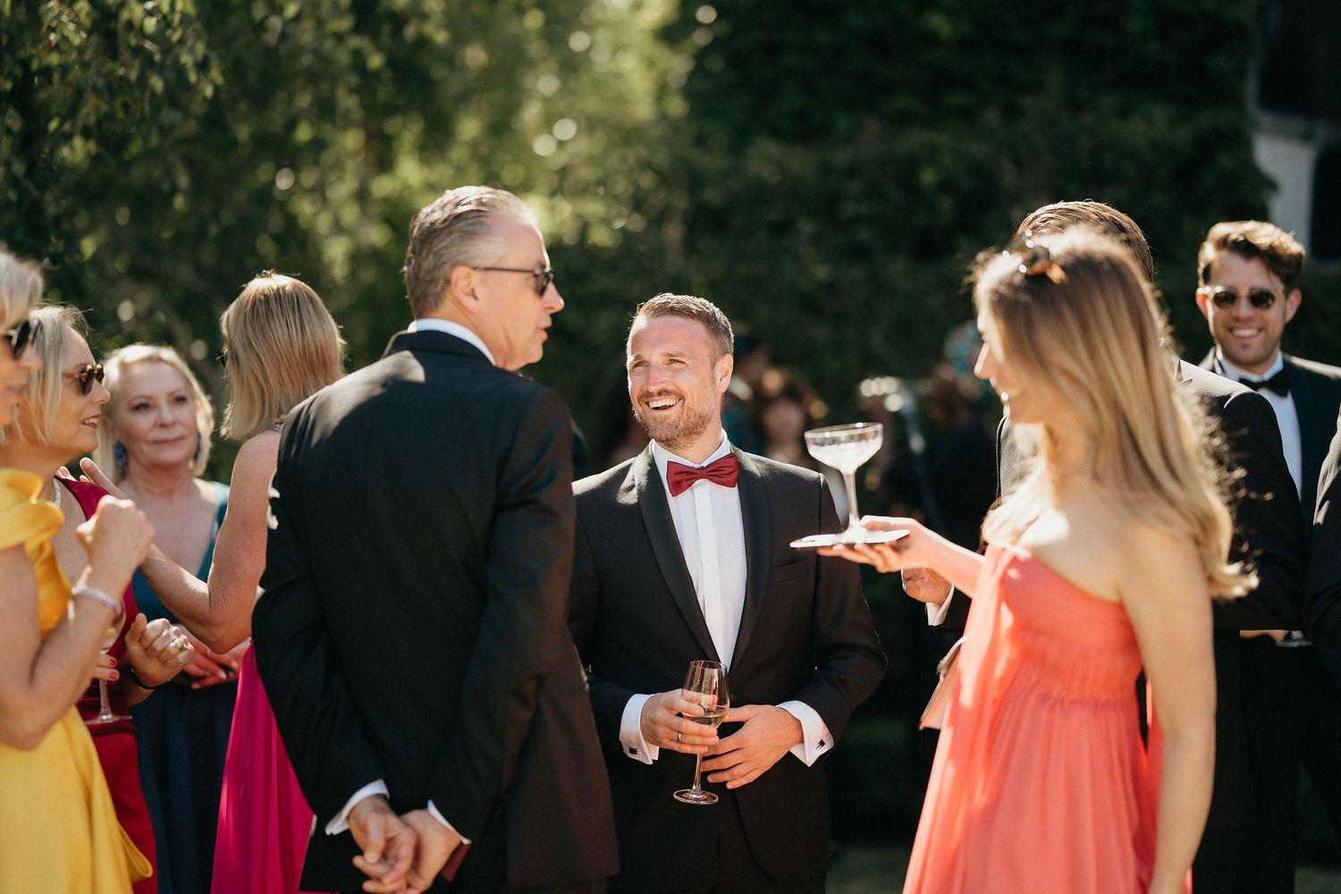 Wedding guests mingle and socialize during an outdoor reception on a sunny afternoon.