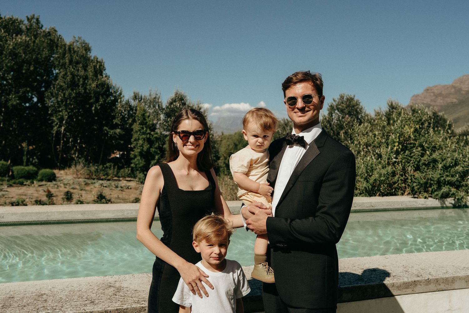 Outdoor wedding reception by a pool with mountains and blue sky visible in the background.