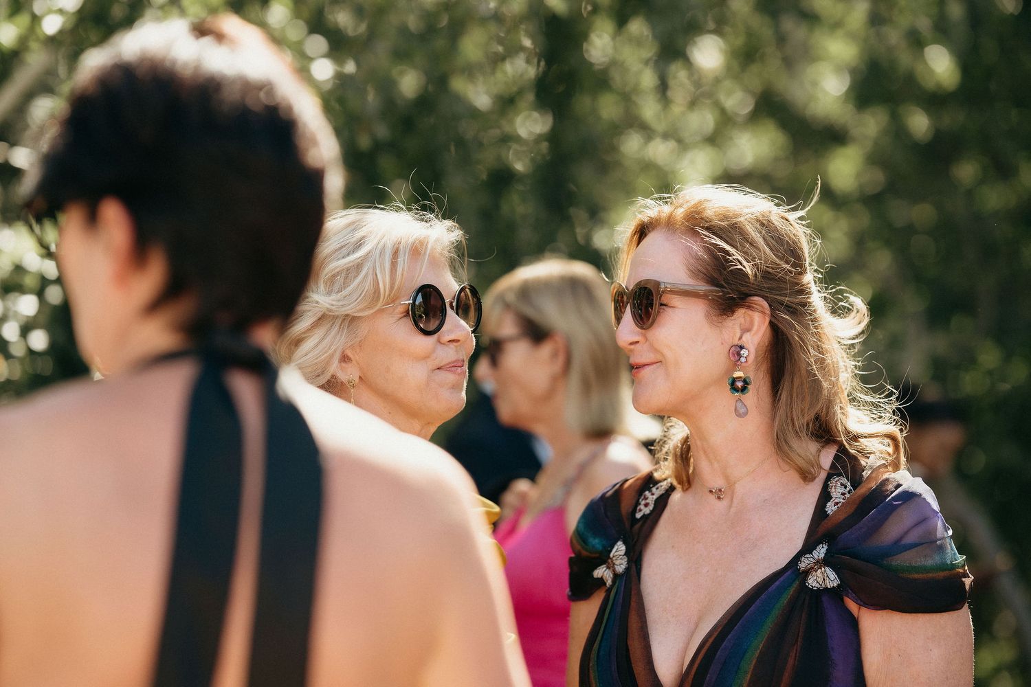 People wearing sunglasses gathered outdoors on a sunny day with soft natural lighting and bokeh effect in background.
