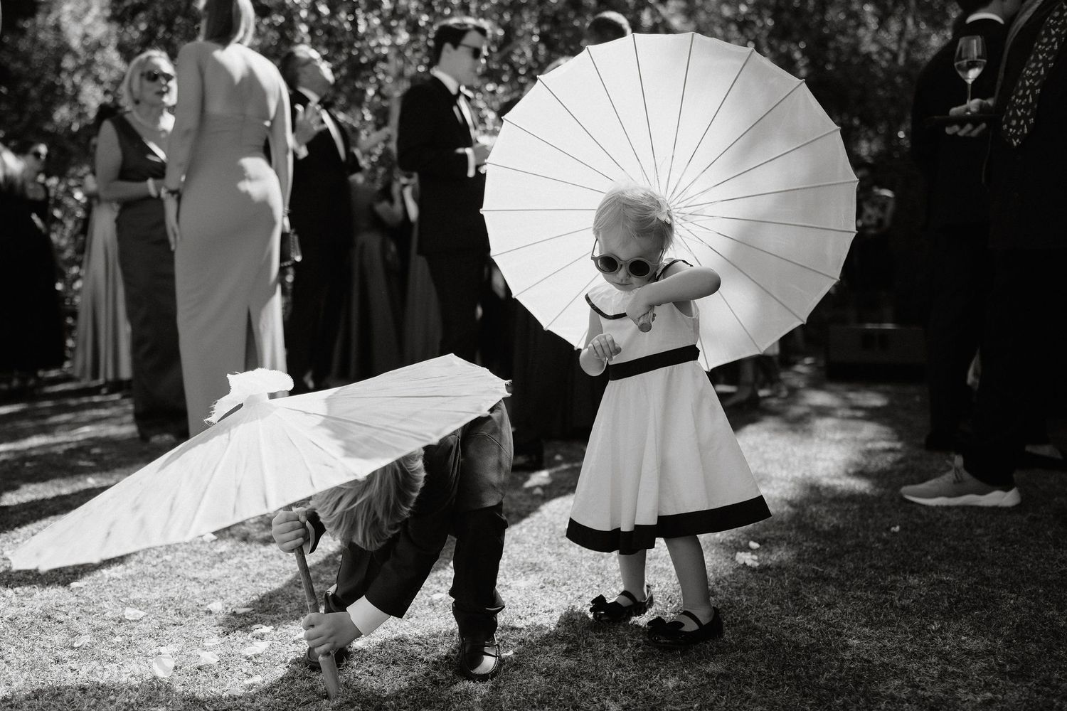Black and white wedding photos featuring parasols and guests in outdoor garden setting.