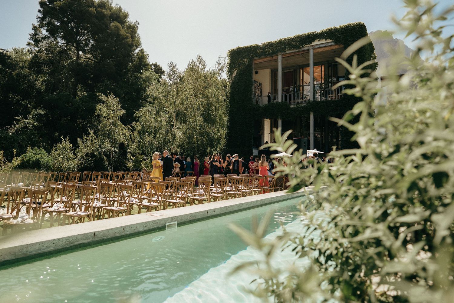 Elegant outdoor wedding ceremony setup with wooden chairs arranged in rows surrounded by lush greenery and trees.
