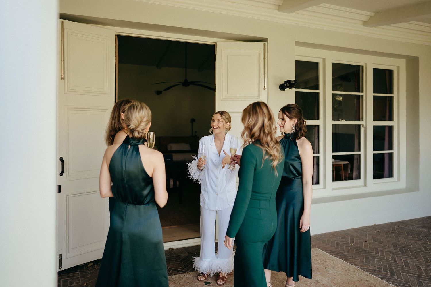 A group of people in formal attire embrace and celebrate together on a covered porch.