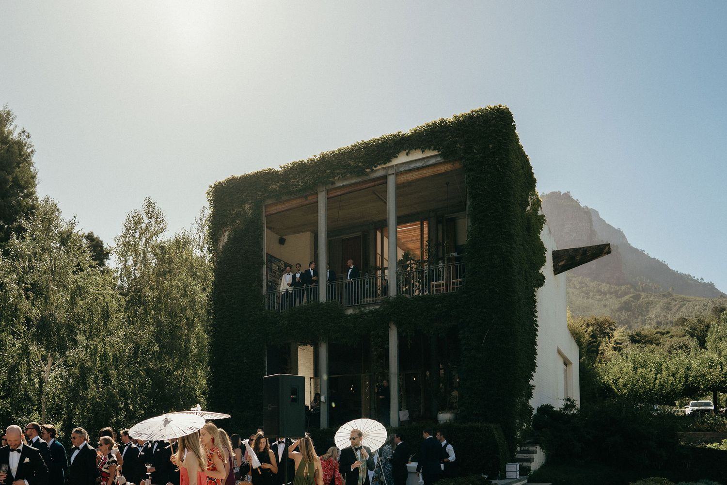 Wedding guests gather on a stone patio surrounded by mountains and desert landscape during an outdoor celebration.