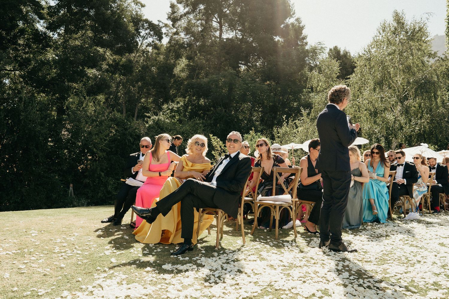 A group of people sit on blankets in a grassy outdoor area enjoying a picnic gathering on a sunny day.