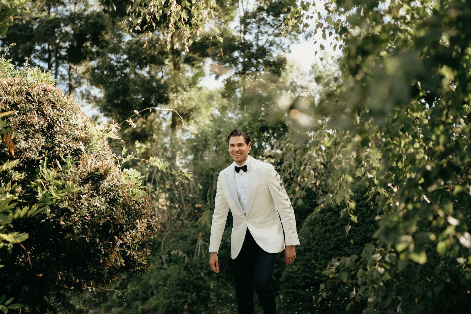 Elegant outdoor wedding ceremony setup with white chairs and floral arrangements in a lush garden setting.