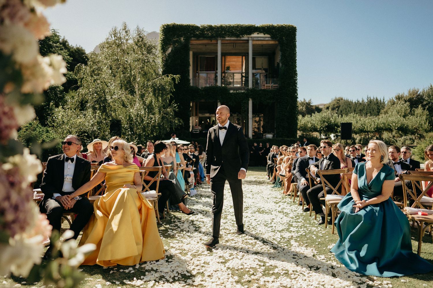 Outdoor wedding ceremony guests seated in white chairs on a sunny beach with ocean views.