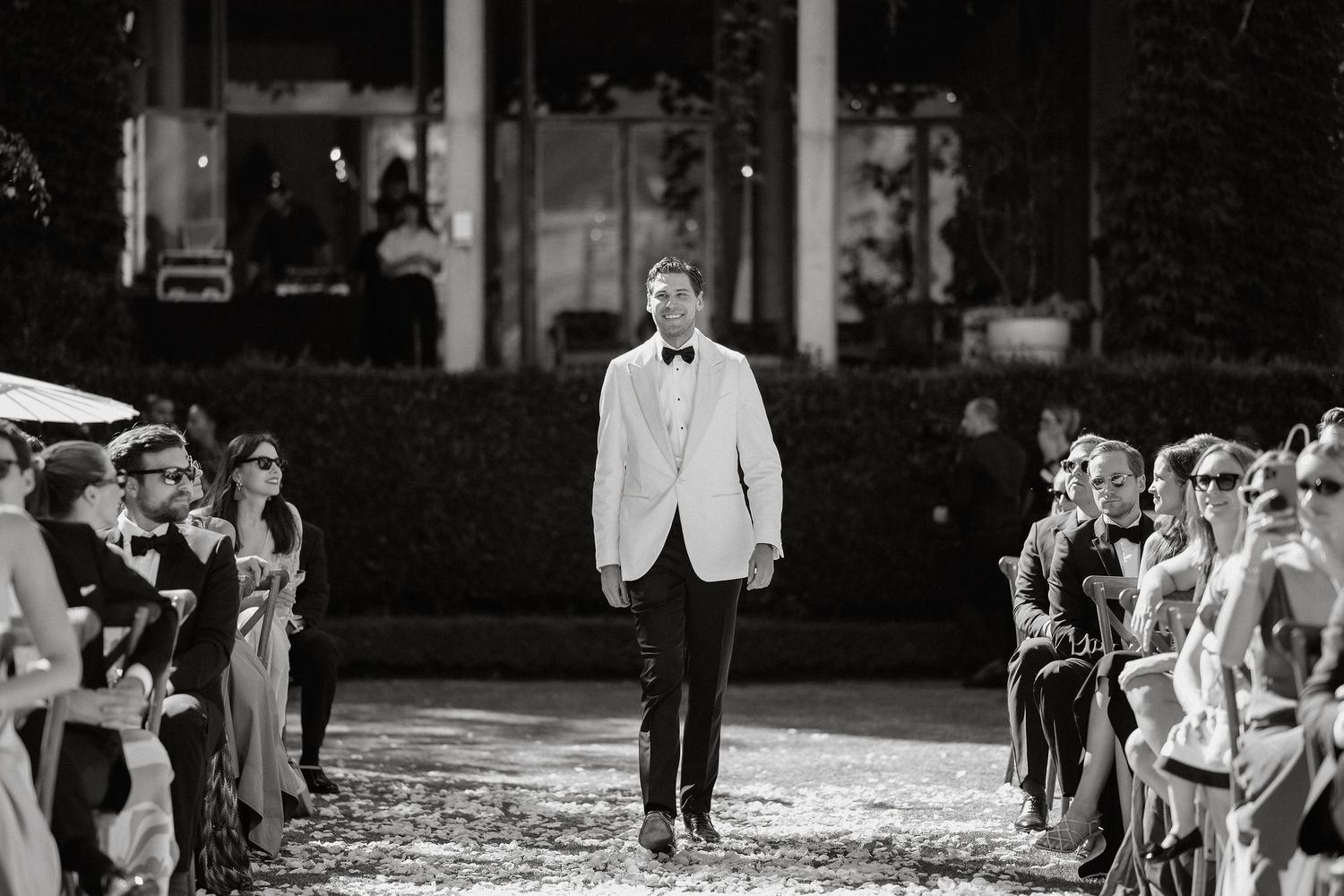 Black and white photo of wedding guests seated in rows during an outdoor ceremony at a historic venue.